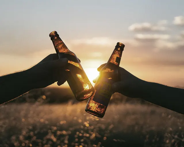 Zwei Bierflaschen stoßen im Sonnenuntergang an